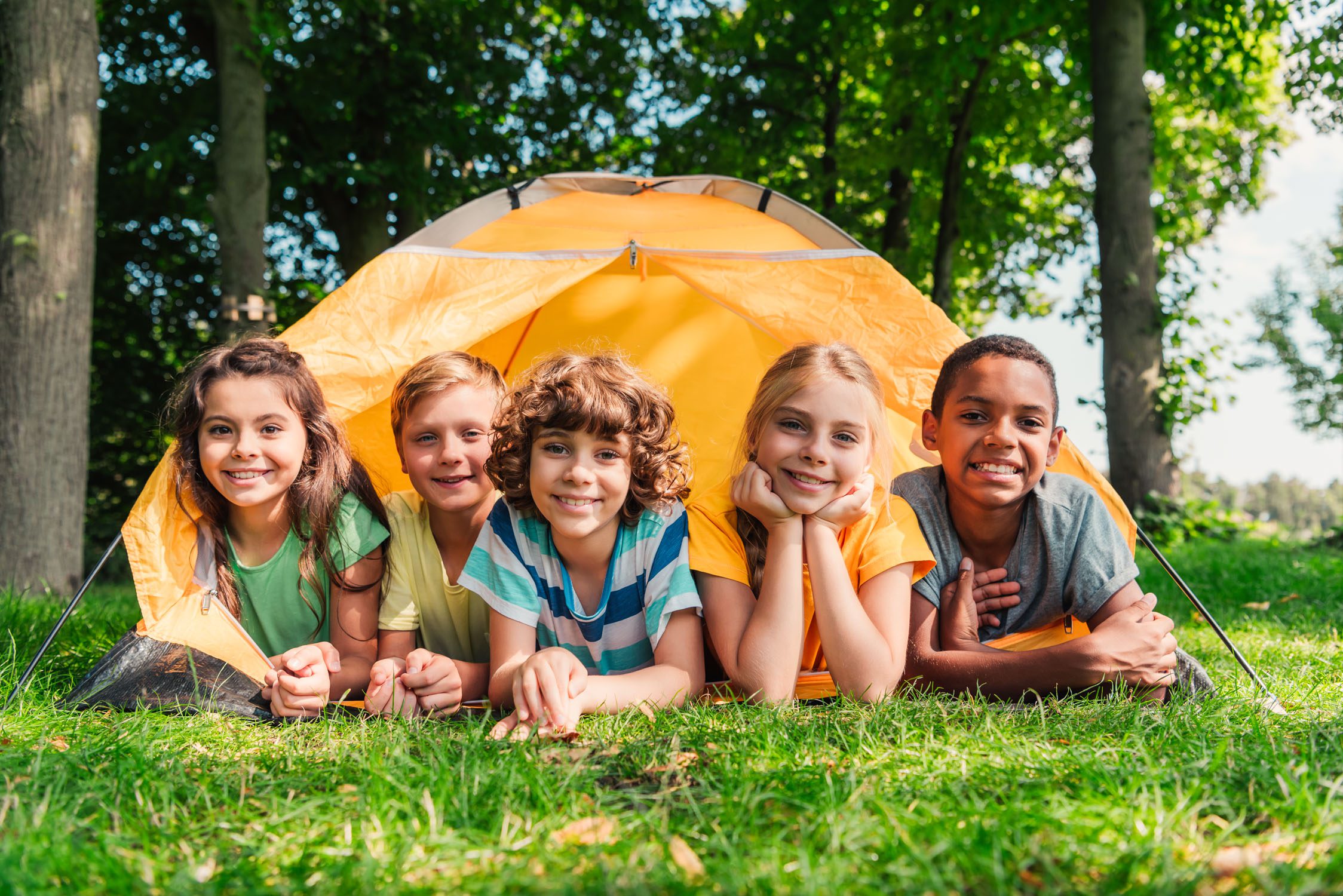 Group photo of cheerful kids smiling by a tent